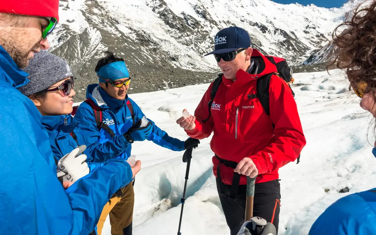 A guided group in crampons on the Tasman Glacier with the Southern Alps behind