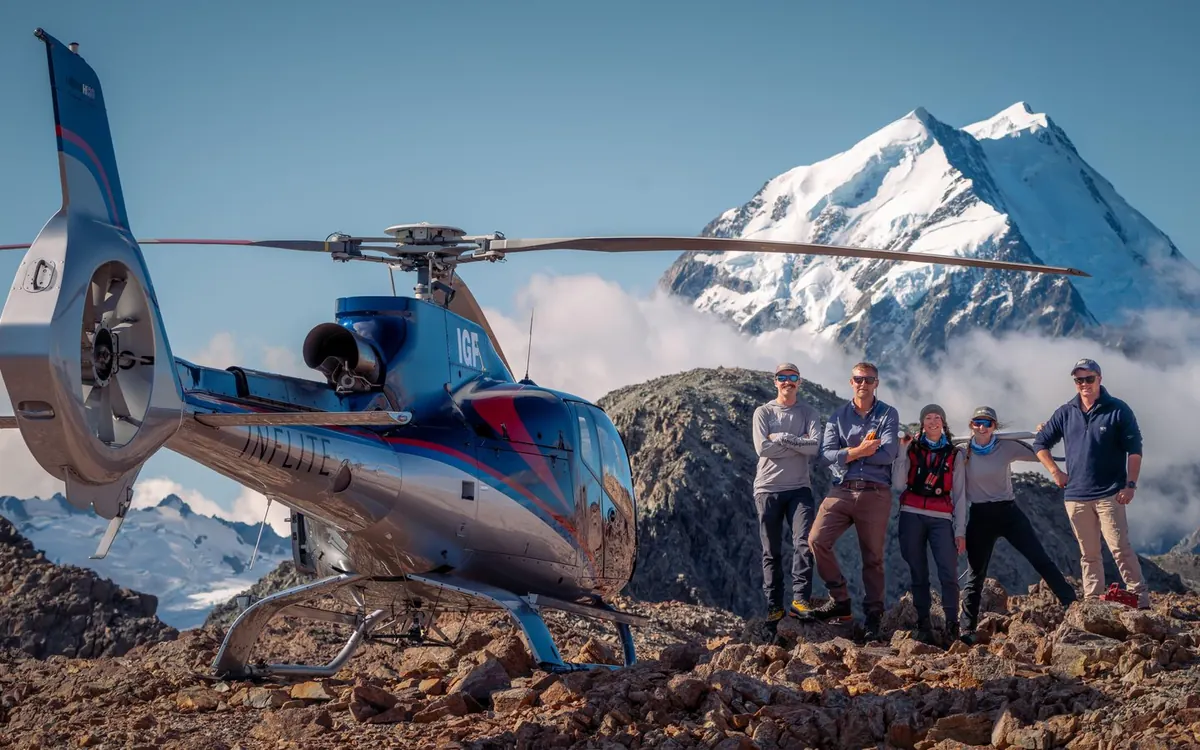 A helicopter landed high on a ridge in the Southern Alps with Aoraki behind it