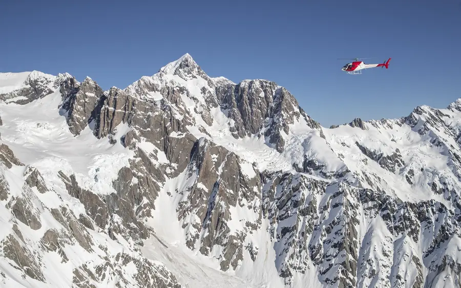 A helicopter flying over the snow and rock of the Southern Alps
